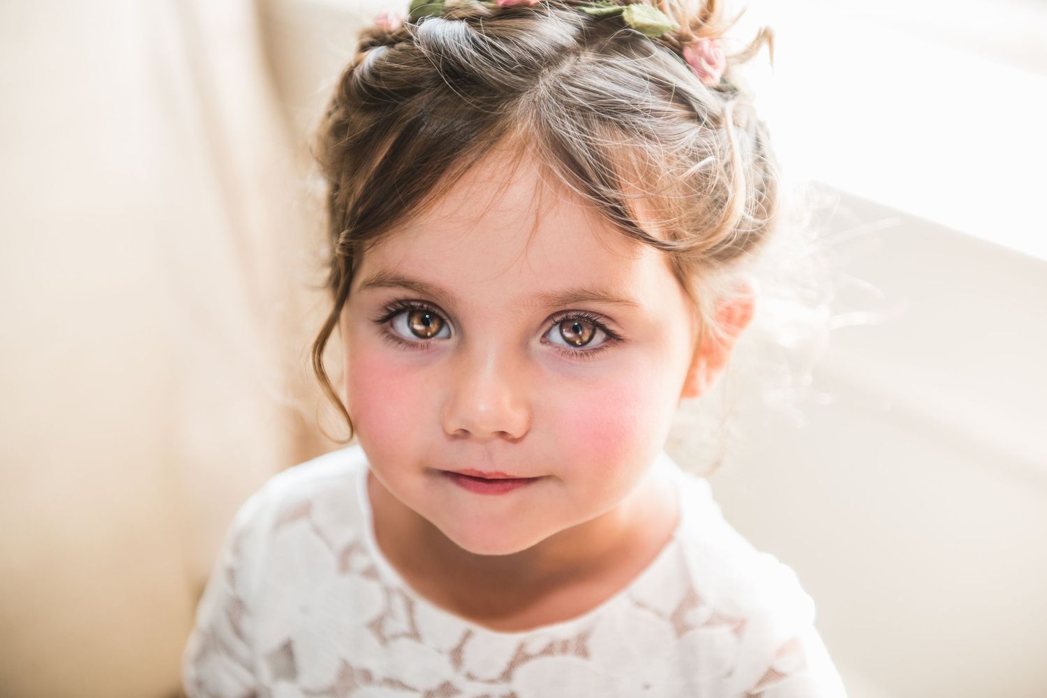 Little Girl Looks at Viewer with Stunning Brown Eyes in Front of a Window and Soft Cream Background