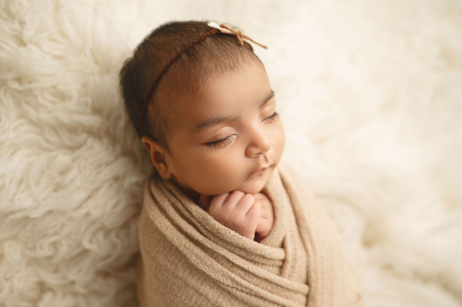 Newborn photography session featuring baby wrapped in soft tan fabric.