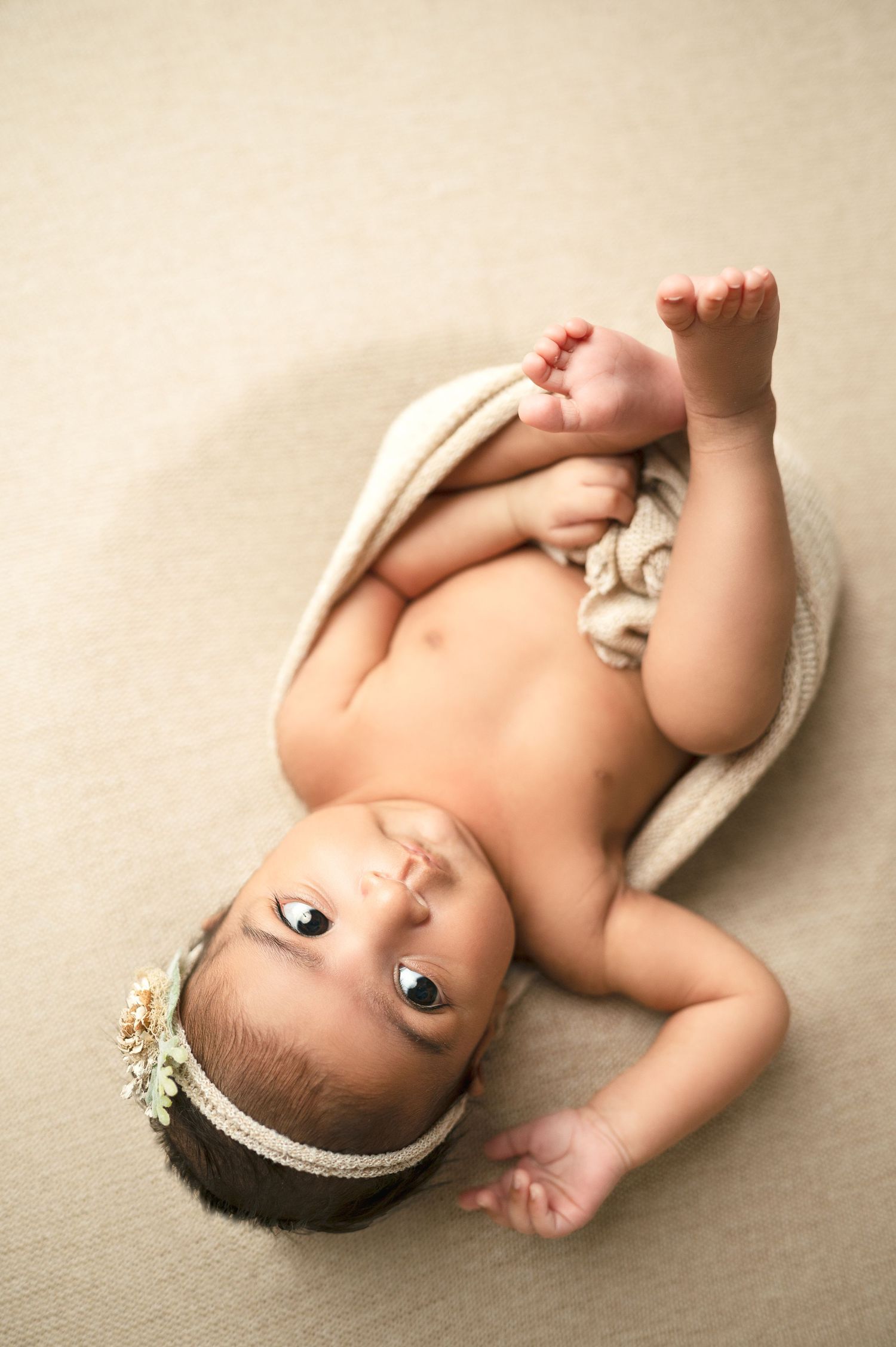 Side view of infant wearing delicate headband on cream backdrop.