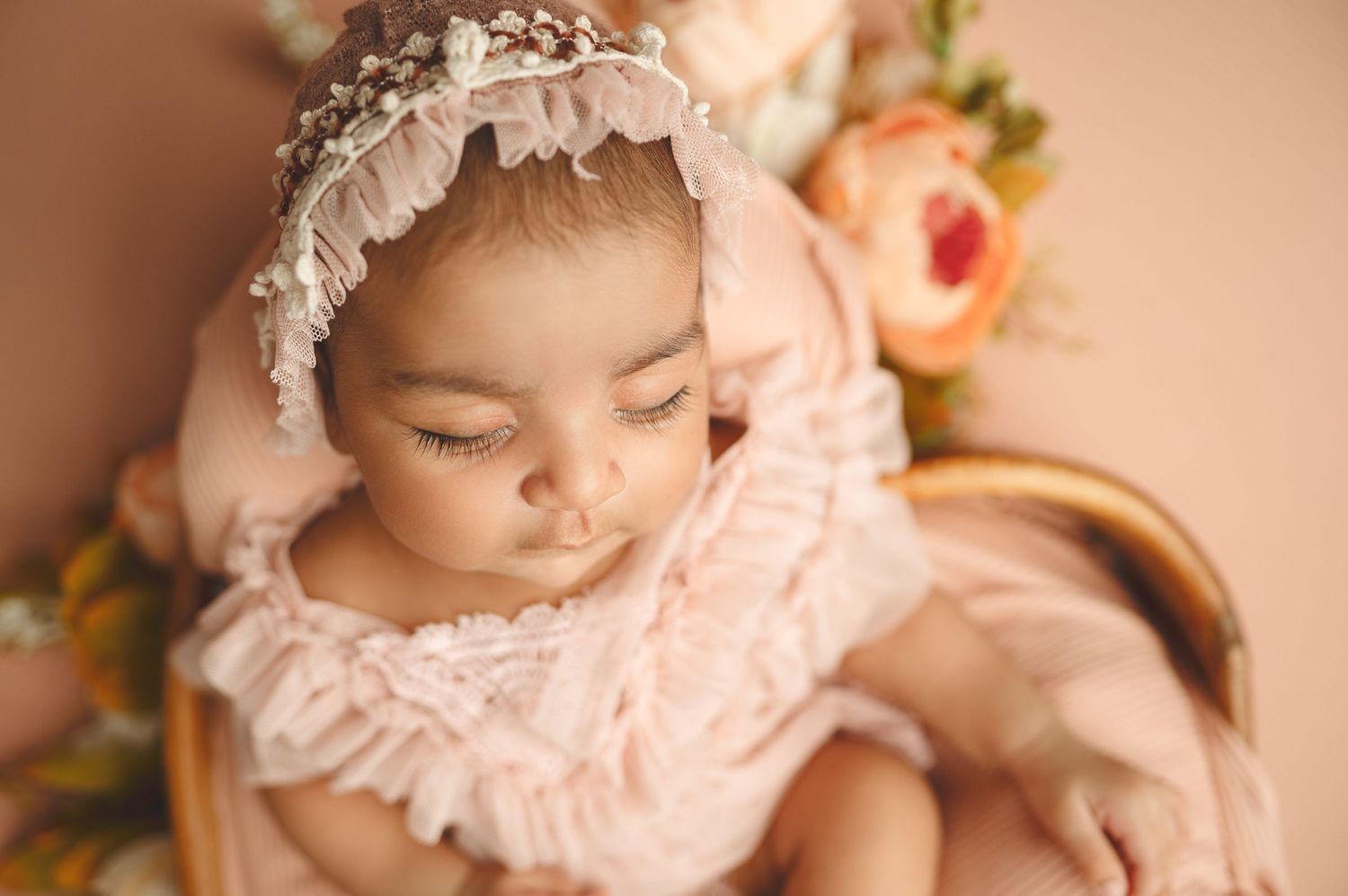 Sleeping baby in pink lace outfit surrounded by delicate floral accents.