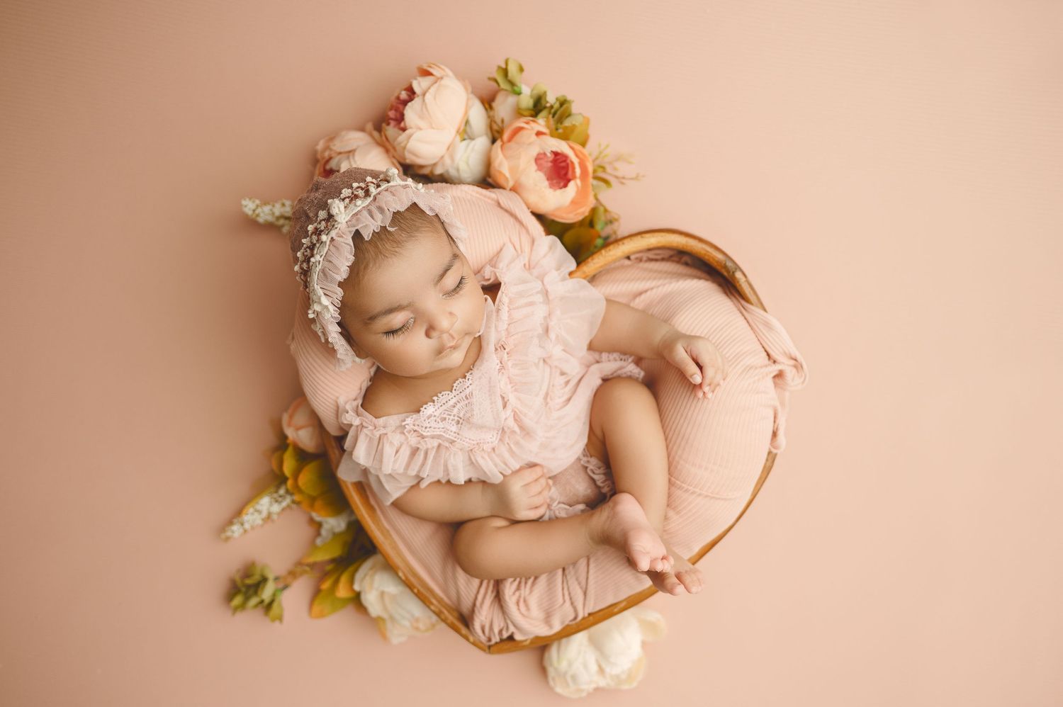 Newborn sleeping peacefully in pink dress with floral decorations.