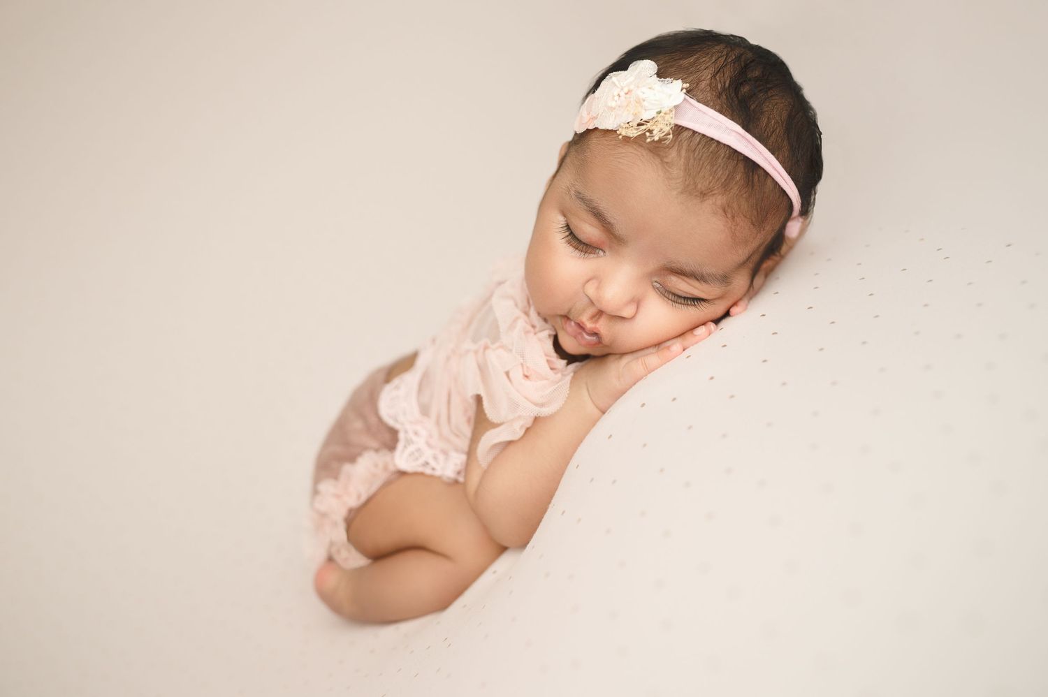 Professional newborn photography with white headband against neutral backdrop.