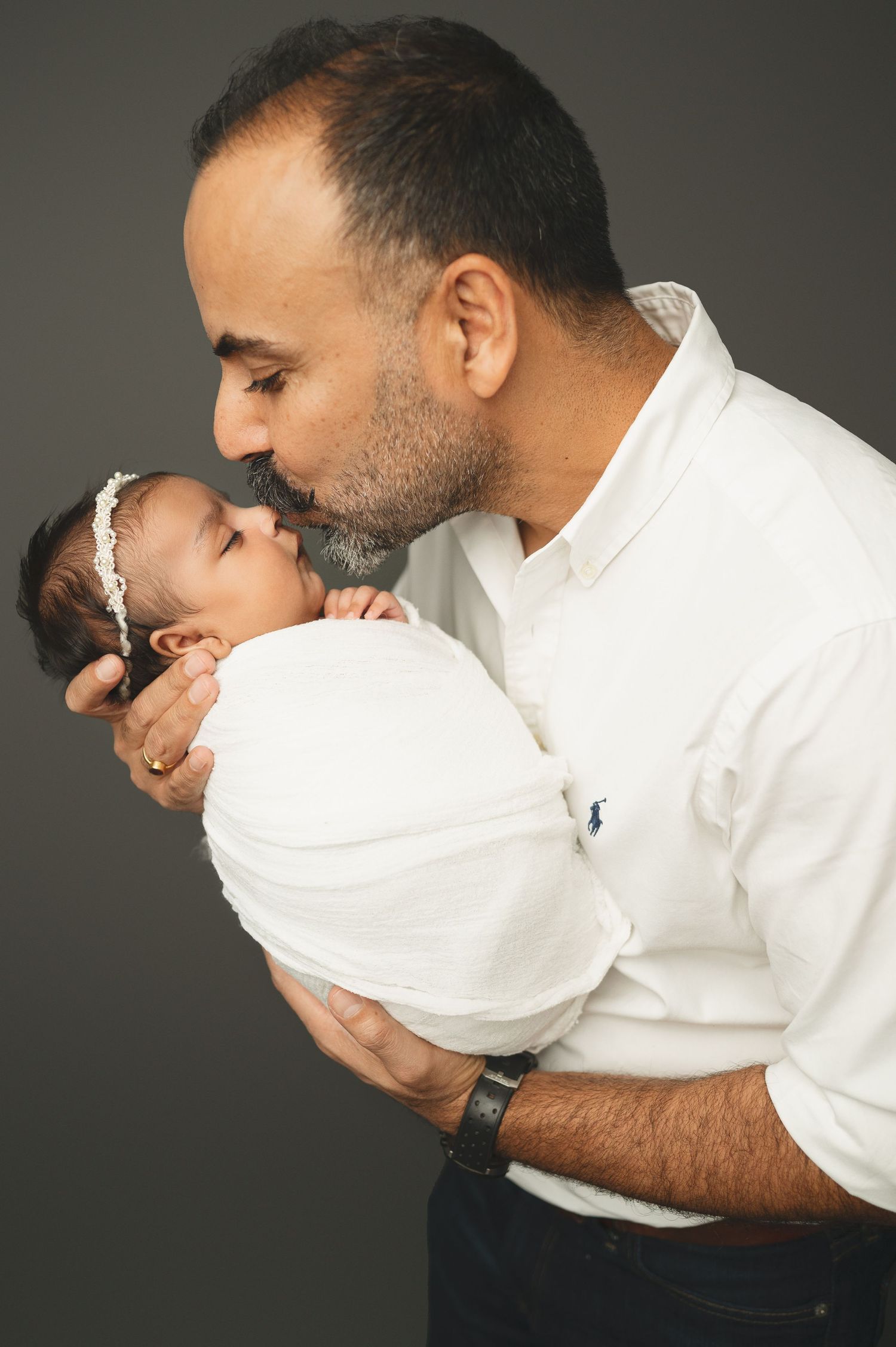 Intimate close-up portrait of parent in white shirt tenderly cradling sleeping newborn swaddled in white.