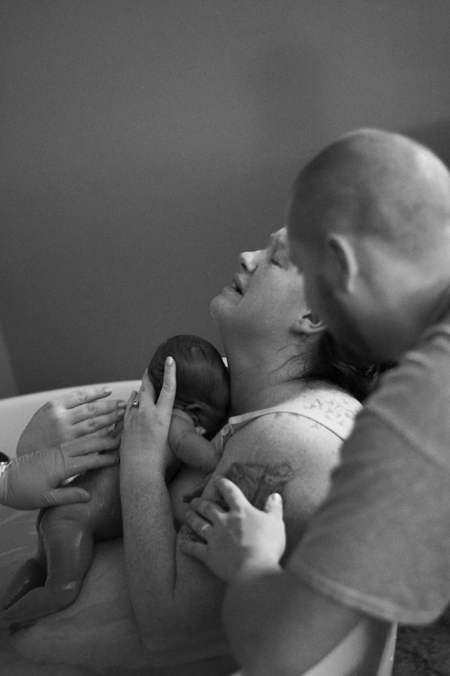 Black and white intimate portrait of parents bonding with newborn baby.
