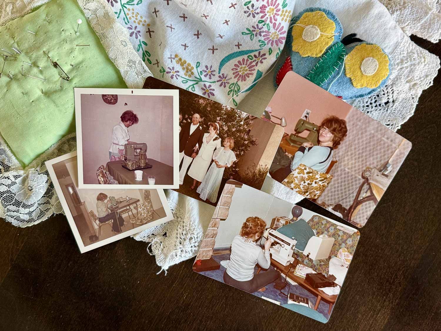 Vintage 1970s family photos scattered on a wooden table alongside antique lace fabric, green cloth, and decorative items.