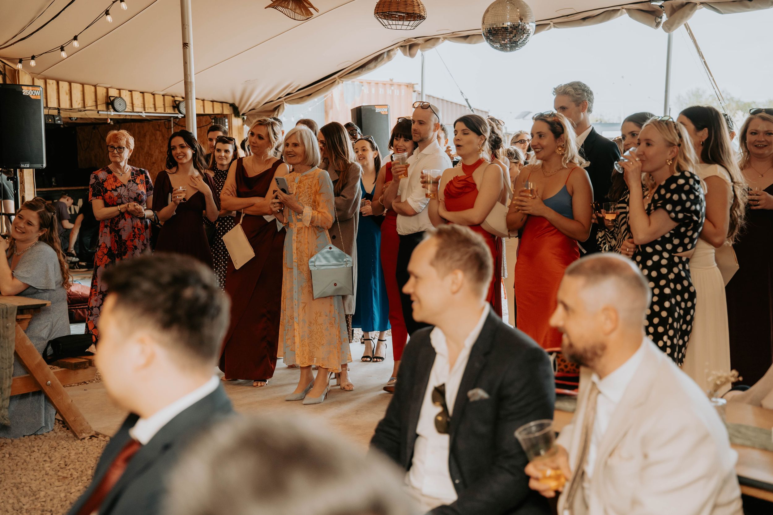 Guests mingling and celebrating at an elegant wedding reception inside a marquee tent with disco ball.