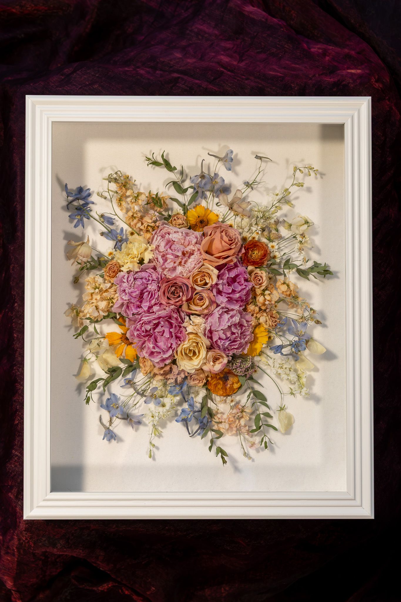Colorful pressed dried flowers arranged in a rustic wooden frame on white background.