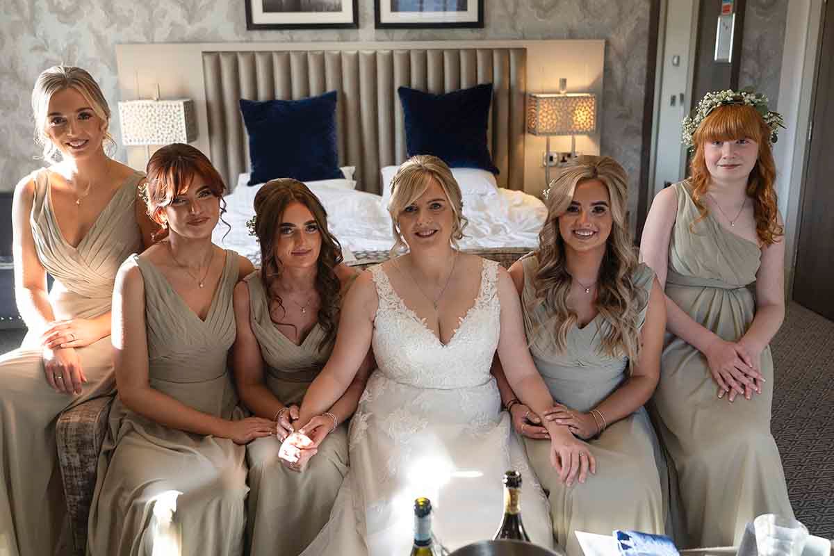 Bride in white lace gown poses with five bridesmaids in champagne dresses in the bridal suite at Hetland Hall wedding venue