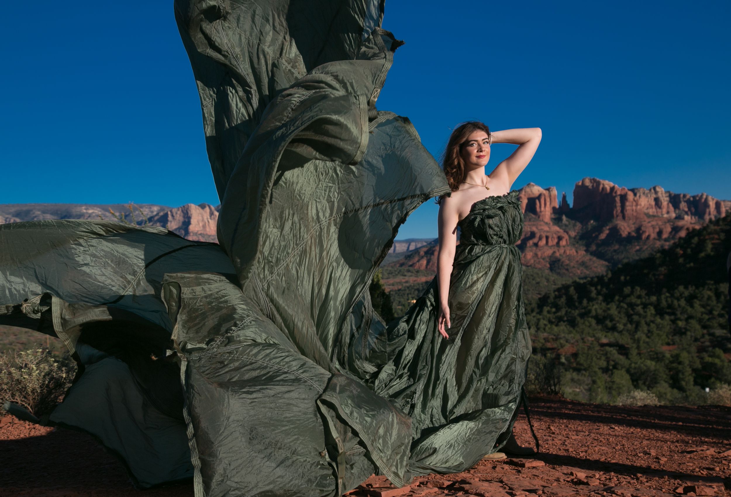 Woman in flowing dark gown poses beside bronze sculpture with red rock Sedona landscape backdrop.