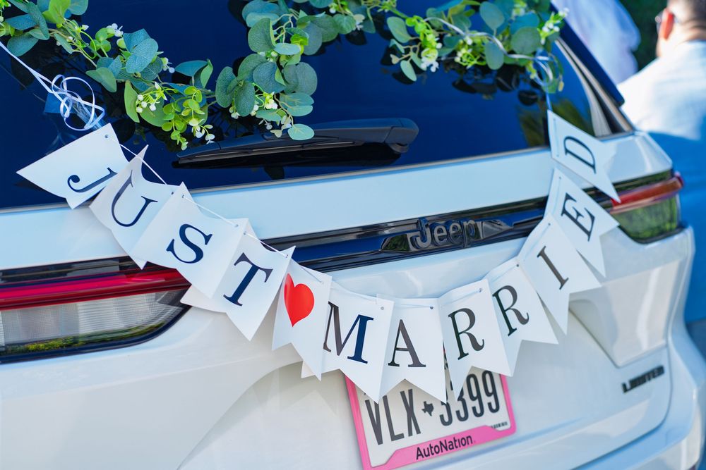 White Jeep decorated with a Just Married banner and greenery garland on the back window for a wedding celebration.