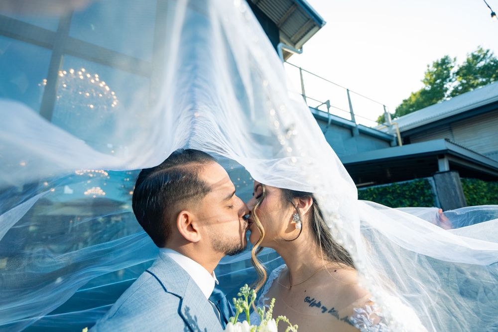 Bride and groom share a romantic kiss under flowing white wedding veil outdoors on their special day.