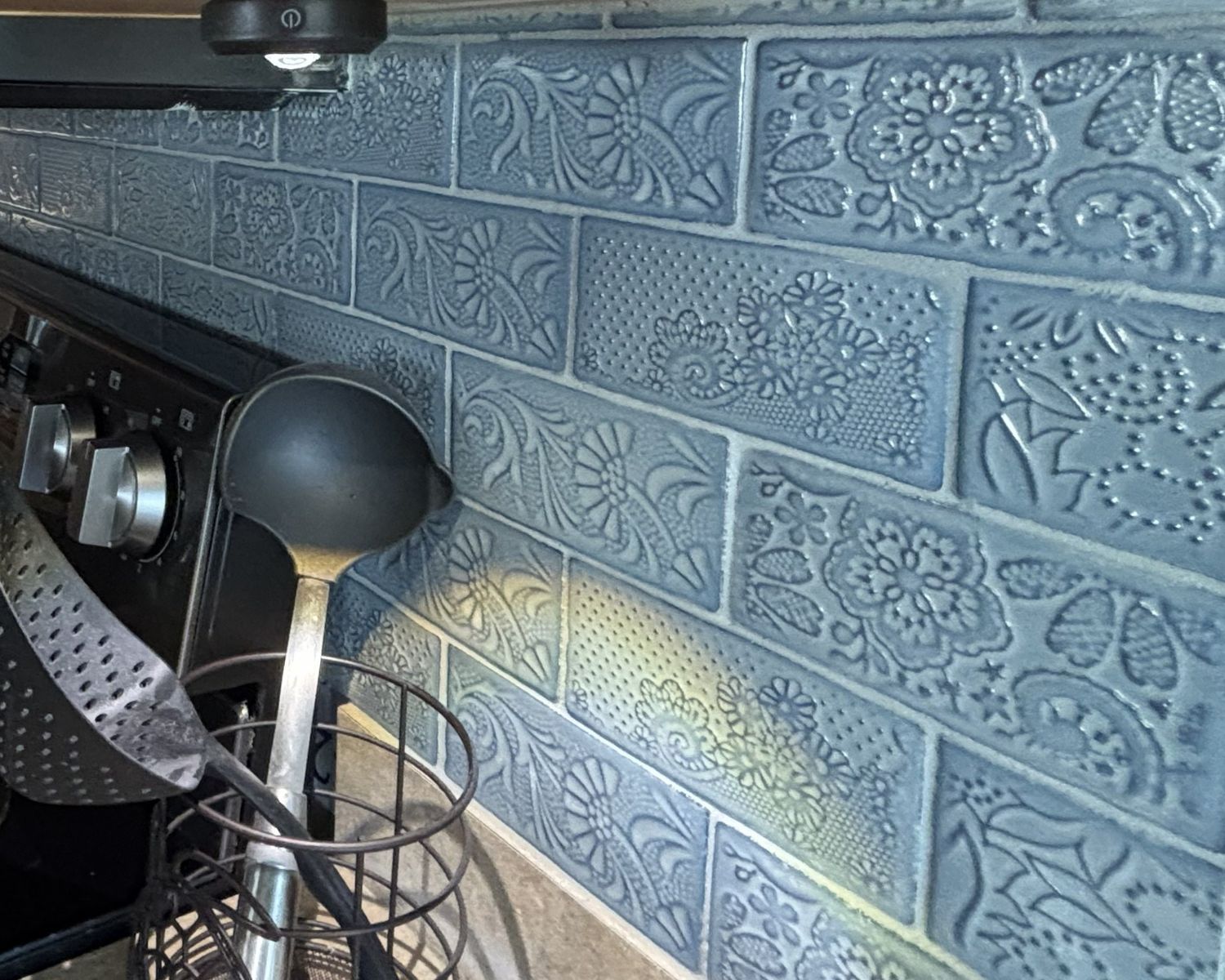Blue embossed floral ceramic brick wall tiles used as a decorative kitchen backsplash.