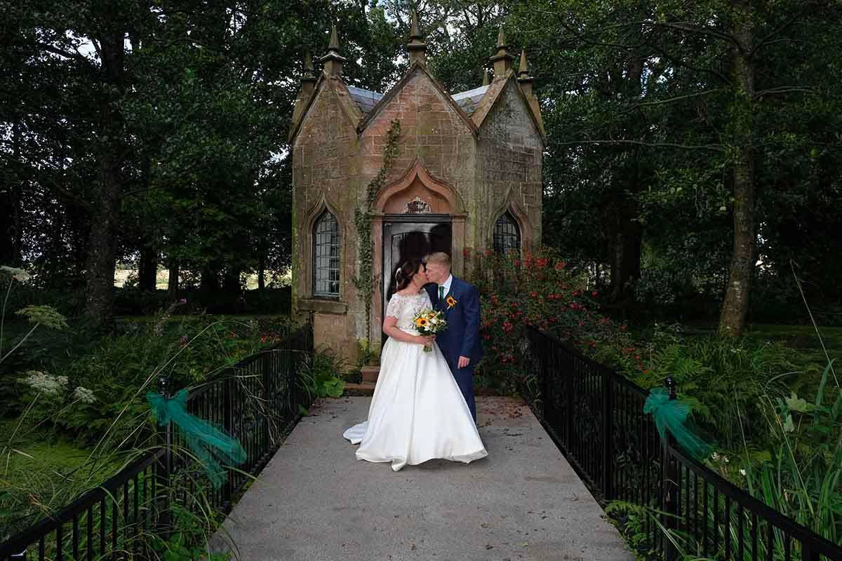 Bride and groom kissing on the bridge in front of the chapel at Blaithwaite House wedding venue near Wigton