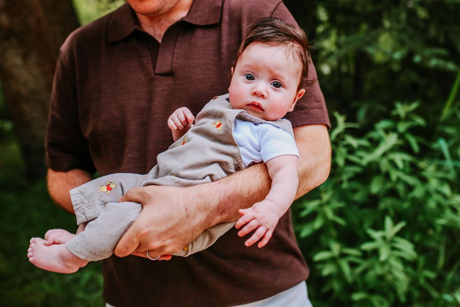 Adult holding a happy baby outdoors in a lush green garden setting.