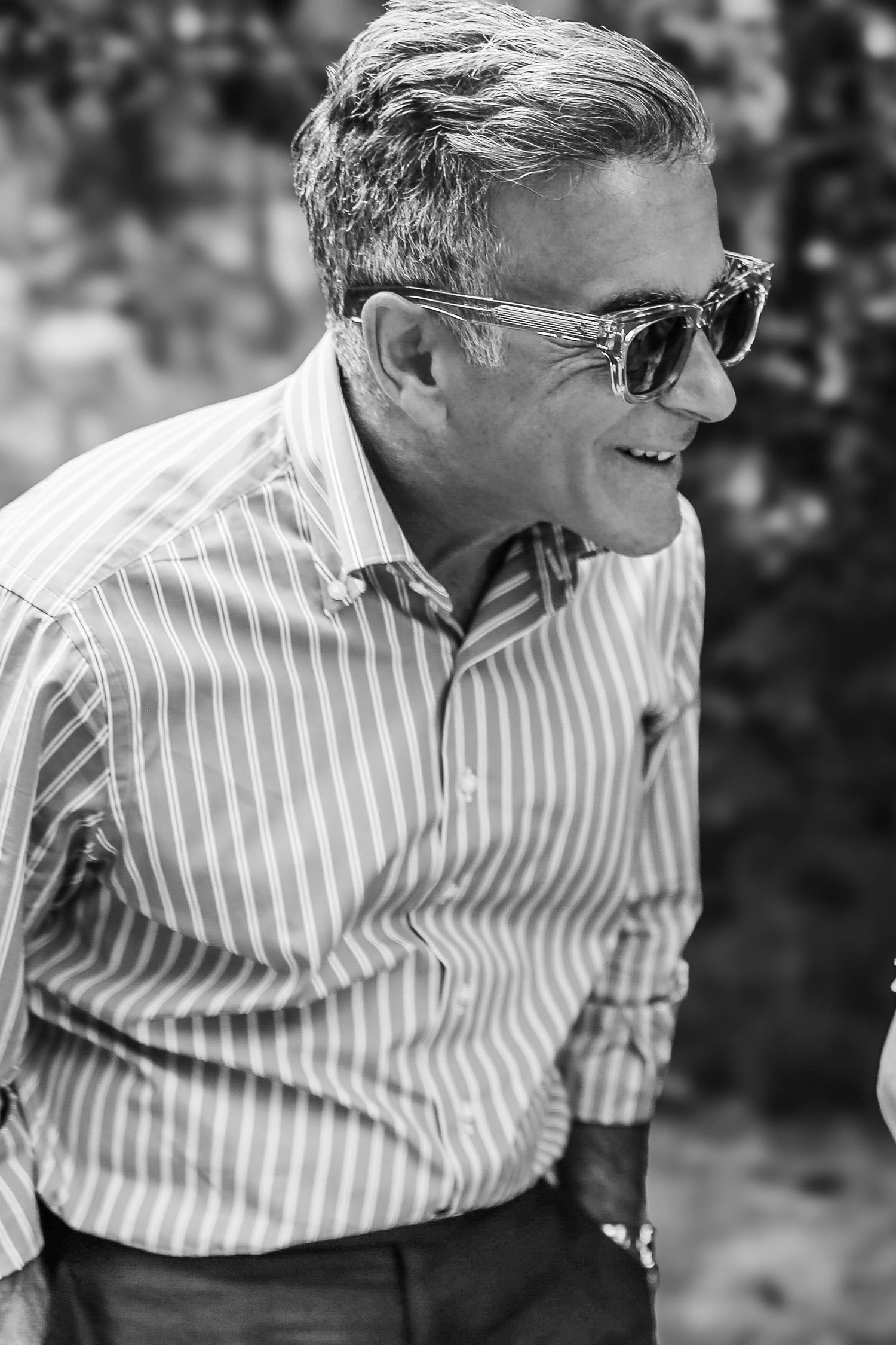 Black and white portrait of a smiling middle-aged man in striped shirt and sunglasses outdoors.
