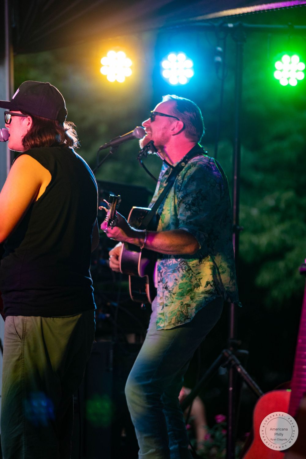 Live outdoor concert with guitarist singing into microphone under colorful stage lights at night.