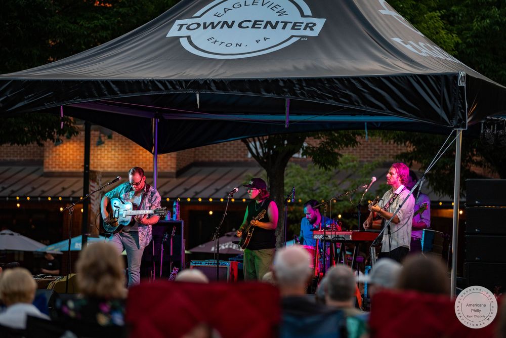 Live band performs outdoors at Eagleview Town Center stage with string lights at dusk.