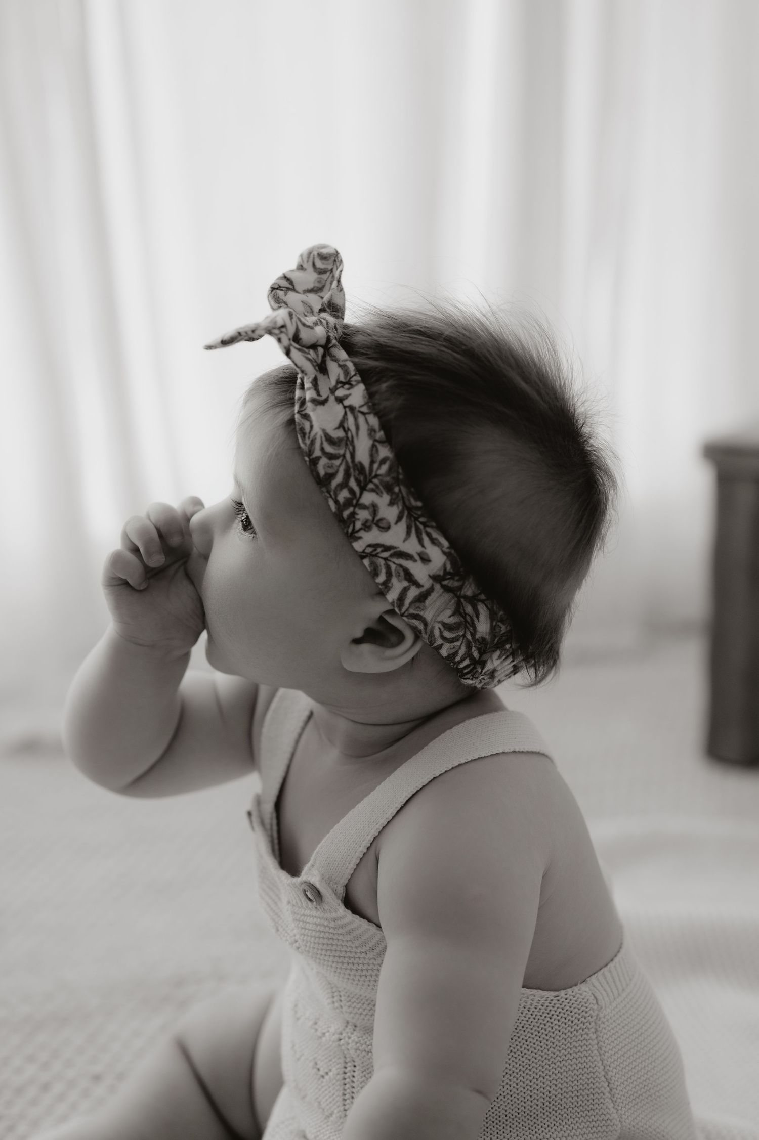 A black and white photo series showing a baby wearing a headband looking upward in four sequential poses.