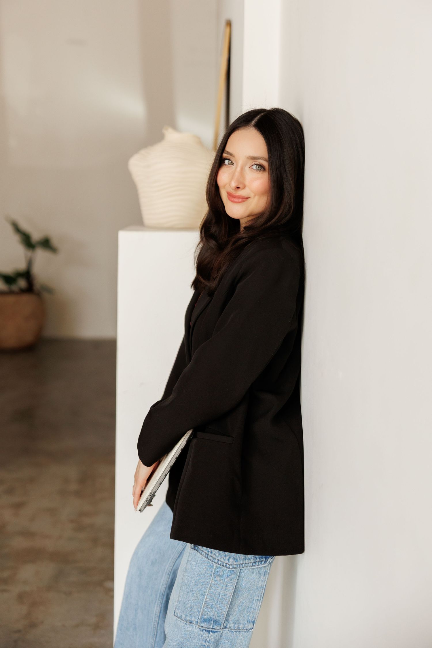 Houston brand photography by Gerry Myers Photo - woman in black blazer and jeans leaning against white wall in bright studio