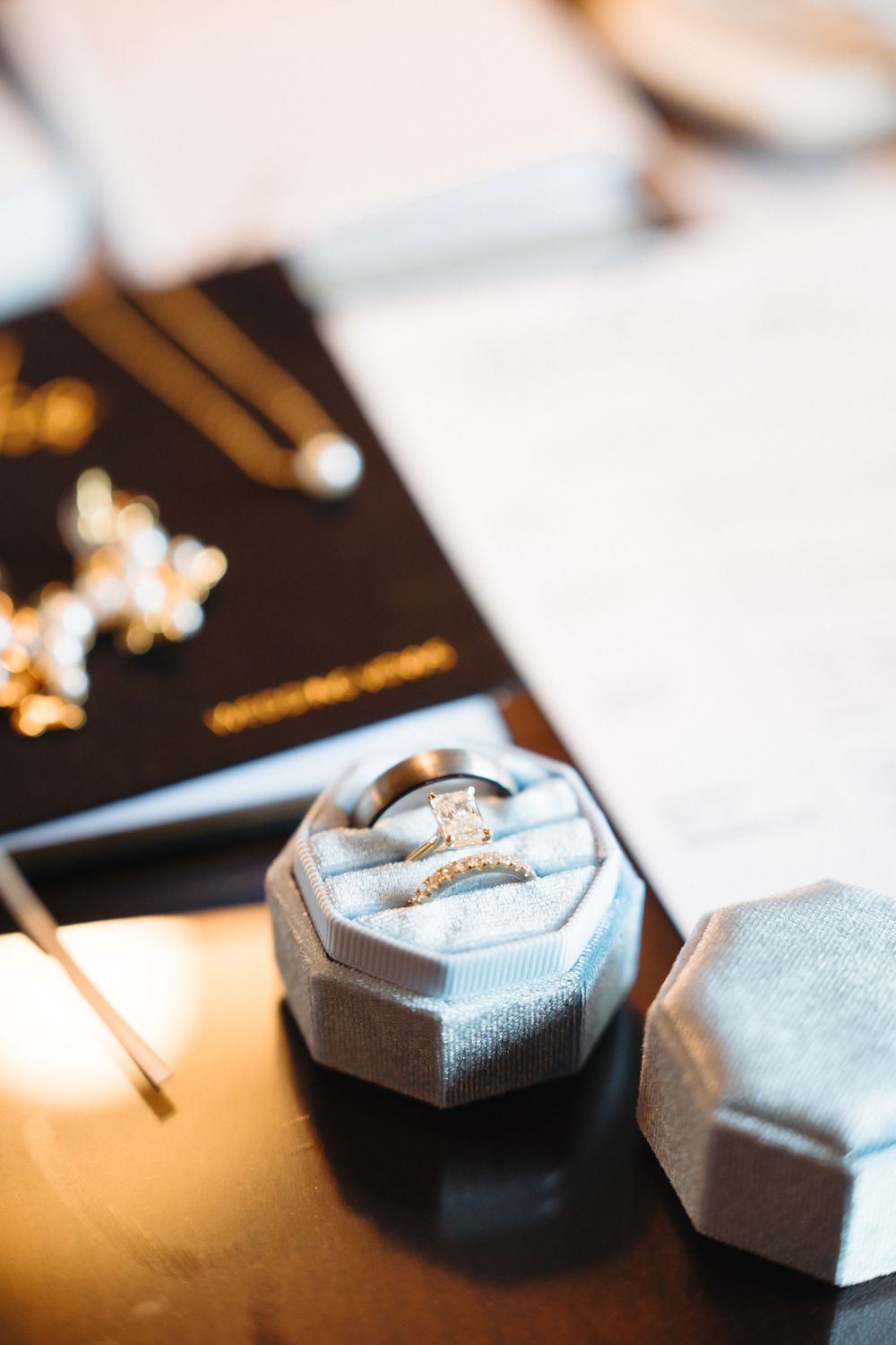Two silver wedding rings displayed in a gray velvet ring box on a wooden table.
