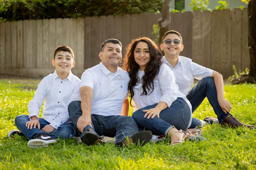 Happy family of four sitting on green grass outdoors in white shirts and jeans.