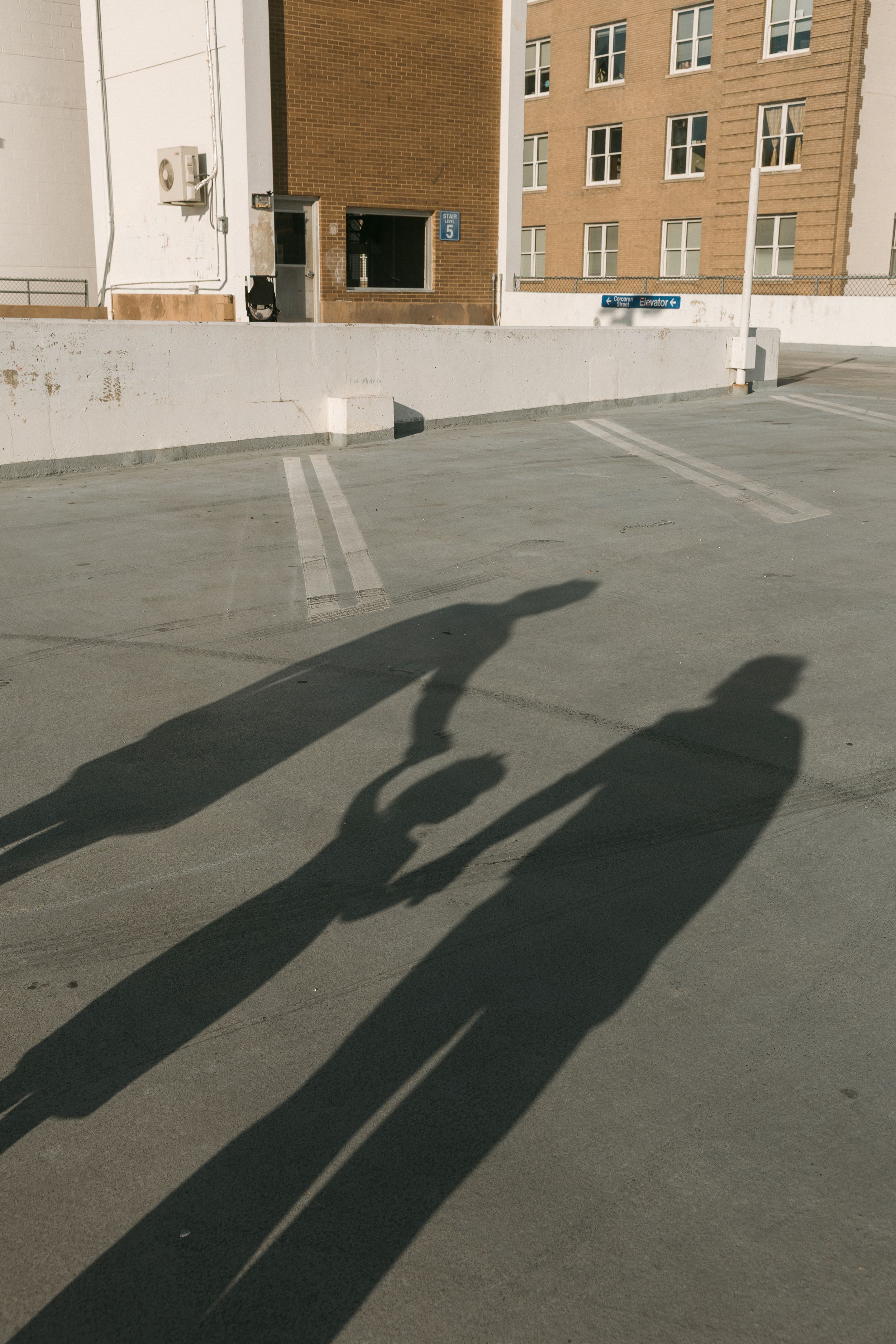 Two elongated shadows of people holding hands cast on a rooftop parking lot with urban buildings in the background.