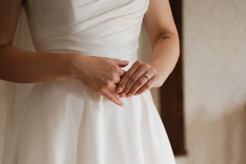Bride in white wedding dress clasping hands together, wearing an elegant ring, close-up detail shot.