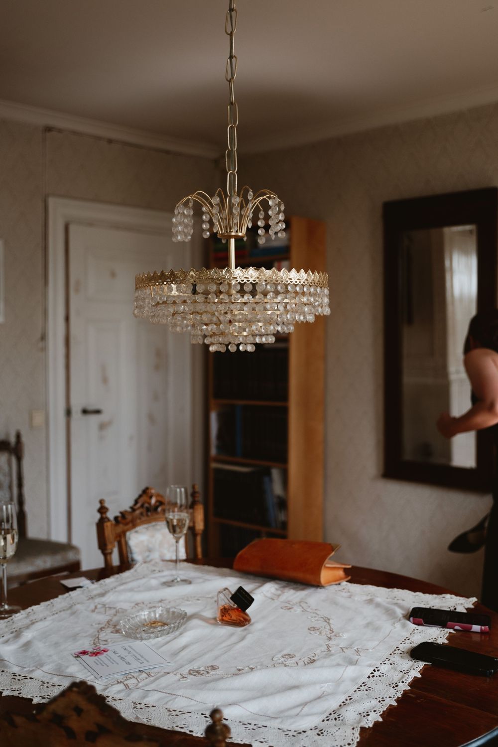 Elegant crystal chandelier hanging above a dining table with lace runner, champagne glasses, and vintage decor.