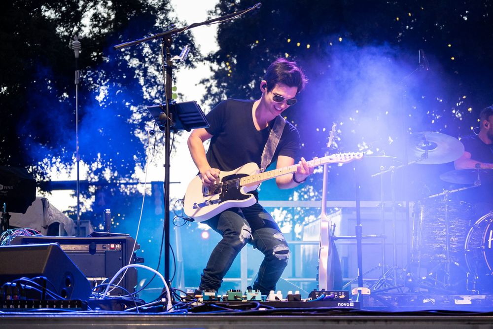 Guitarist performing on stage at outdoor concert with dramatic blue smoke lighting effects.