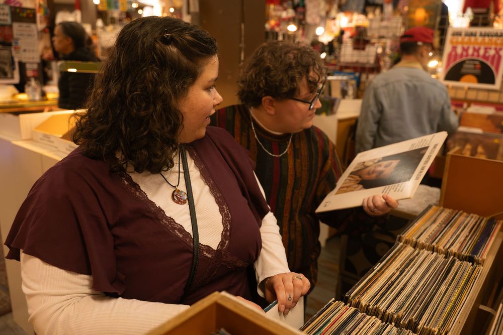 Two women browsing vinyl records in a music store, examining album covers together.