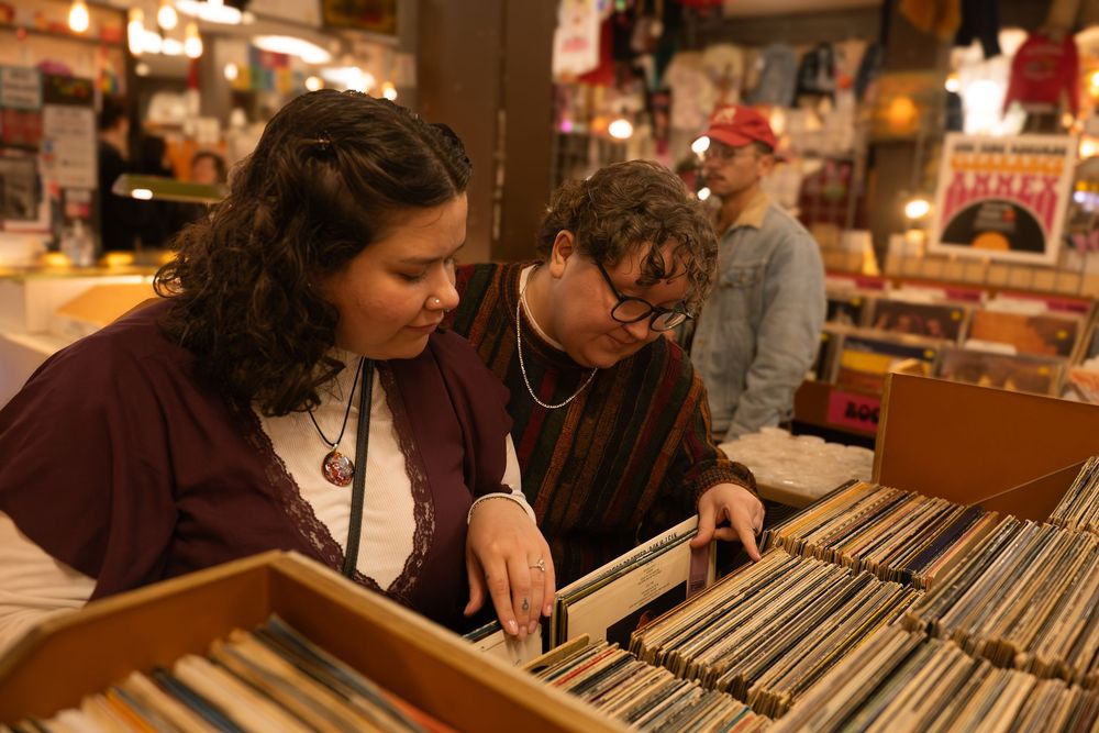 Two women browsing vinyl records at a vintage music store, searching through a large collection of albums.