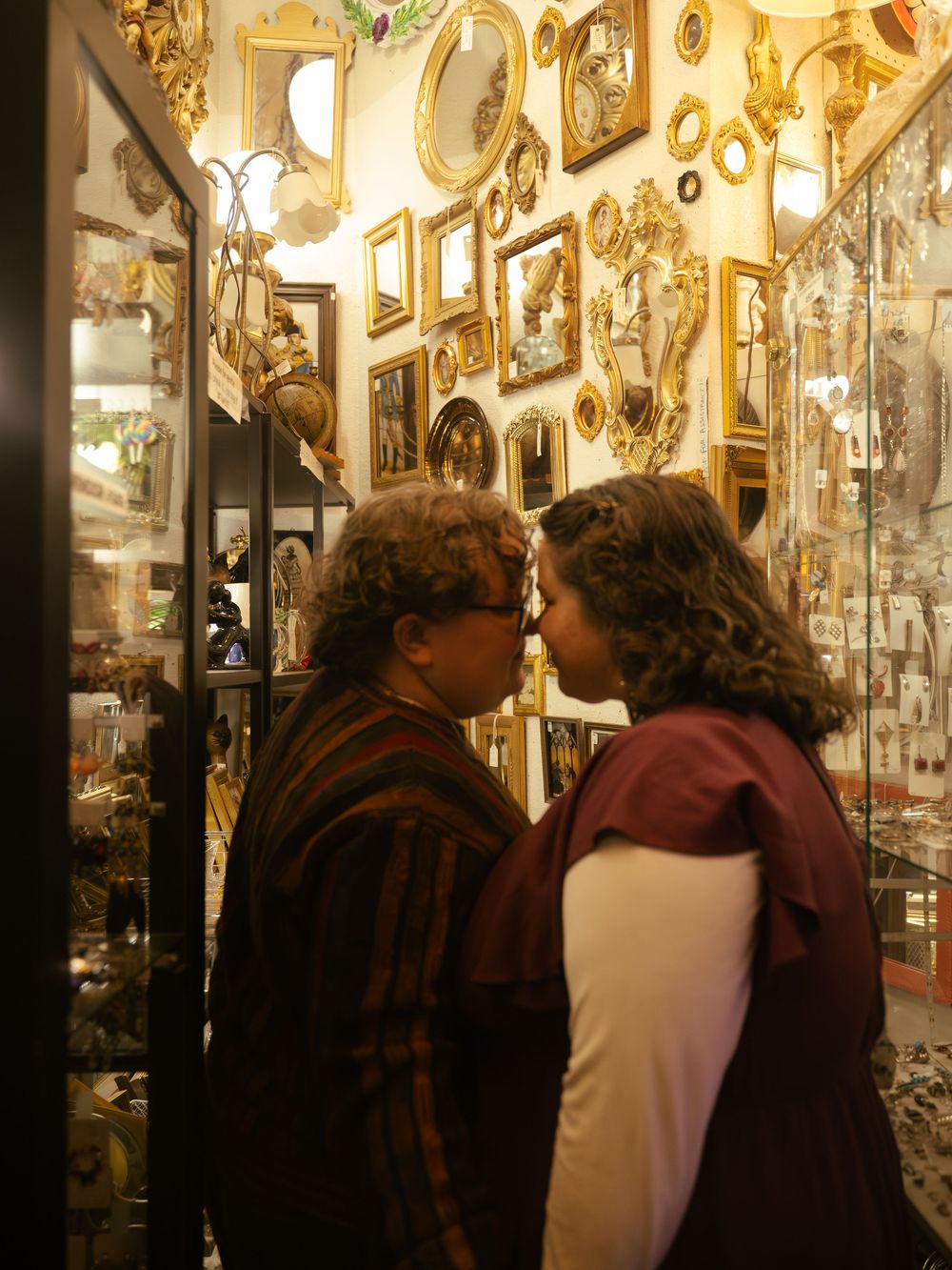 Two people examining antique items in a shop filled with ornate gold mirrors and picture frames on the walls.