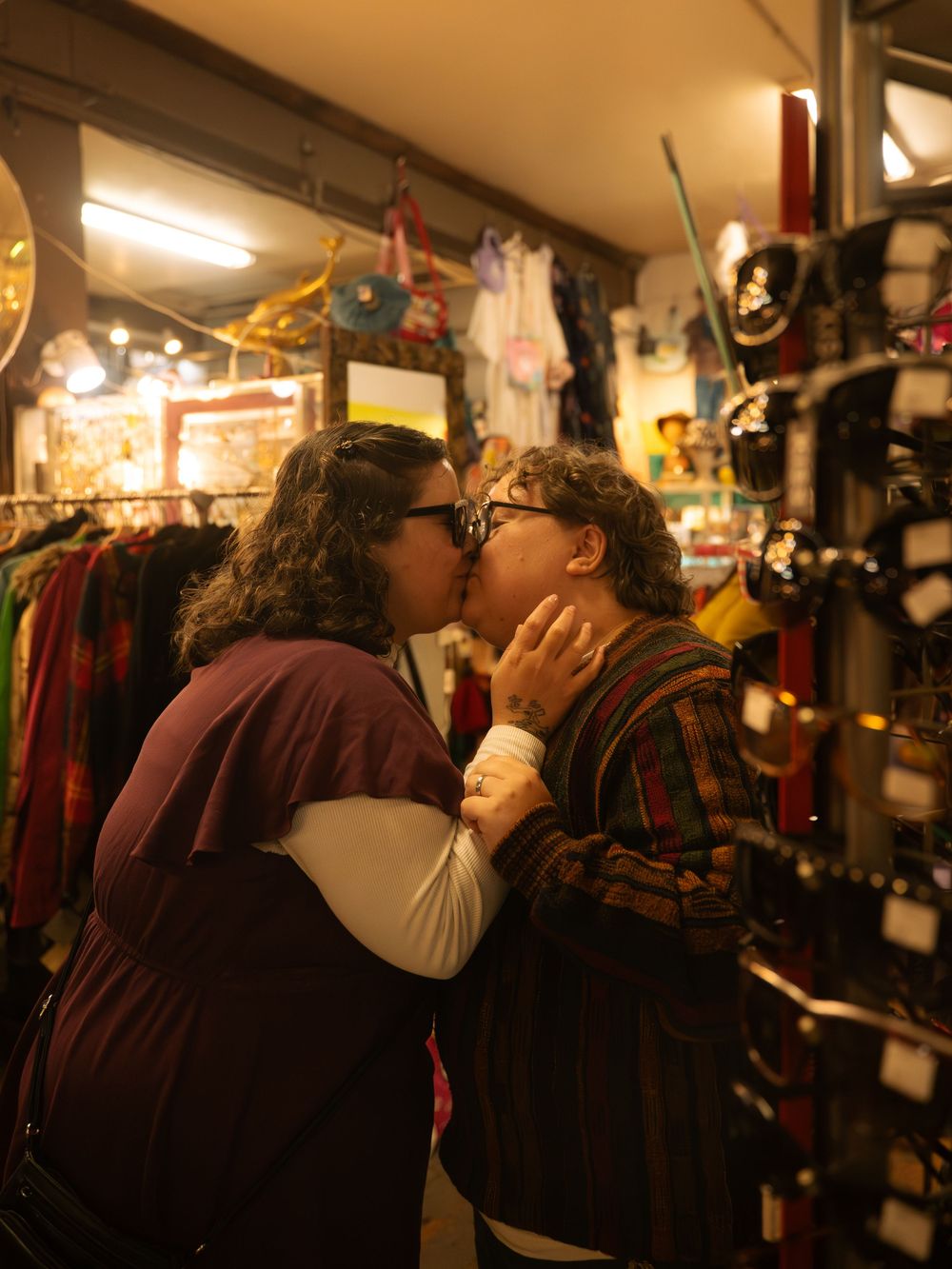 Two people sharing a kiss in a colorful vintage clothing store with racks of clothes and accessories.