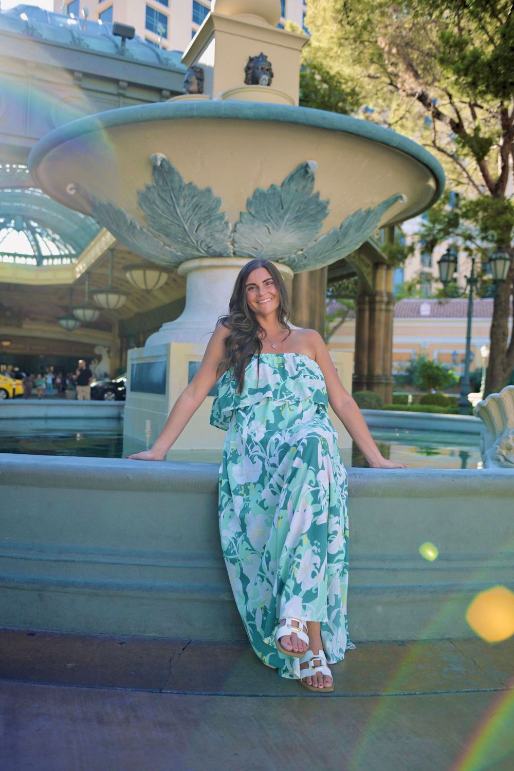 Woman in green floral maxi dress posing by ornate fountain in Las Vegas.