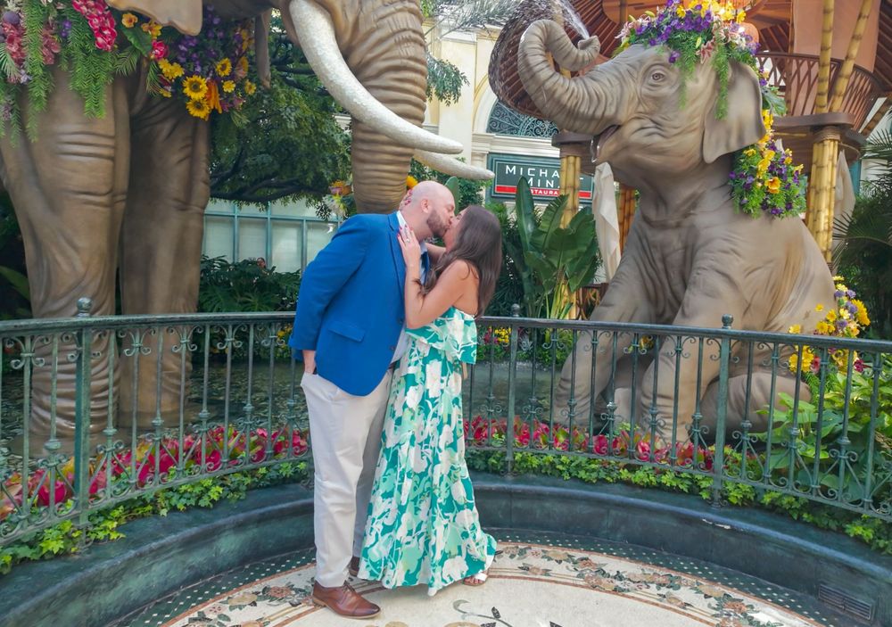 Couple sharing a kiss in front of large elephant statues surrounded by colorful flowers at a Las Vegas resort.