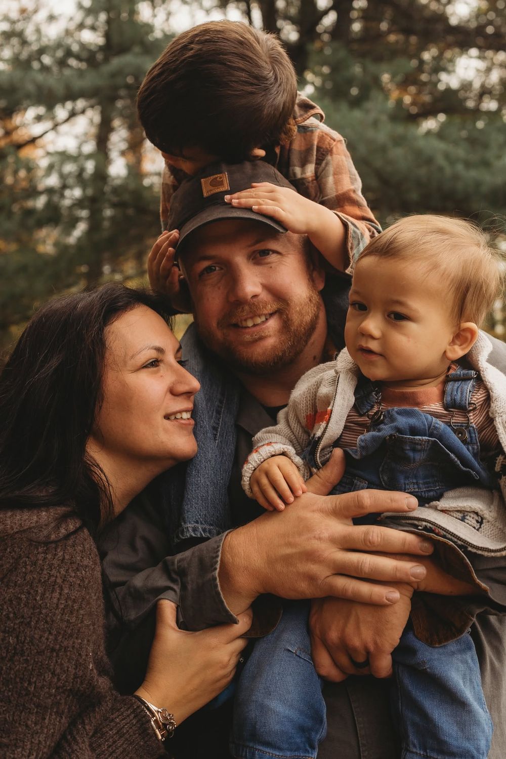 Happy family portrait with parents and two young children embracing outdoors in a forest setting during autumn.