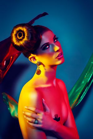 Fashion model illuminated in vibrant red and yellow colored lighting with elegant updo hairstyle and gold earrings.