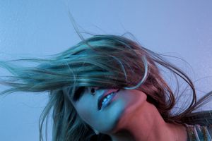 Woman with teal highlighted hair dramatically blowing across her face under blue studio lighting.