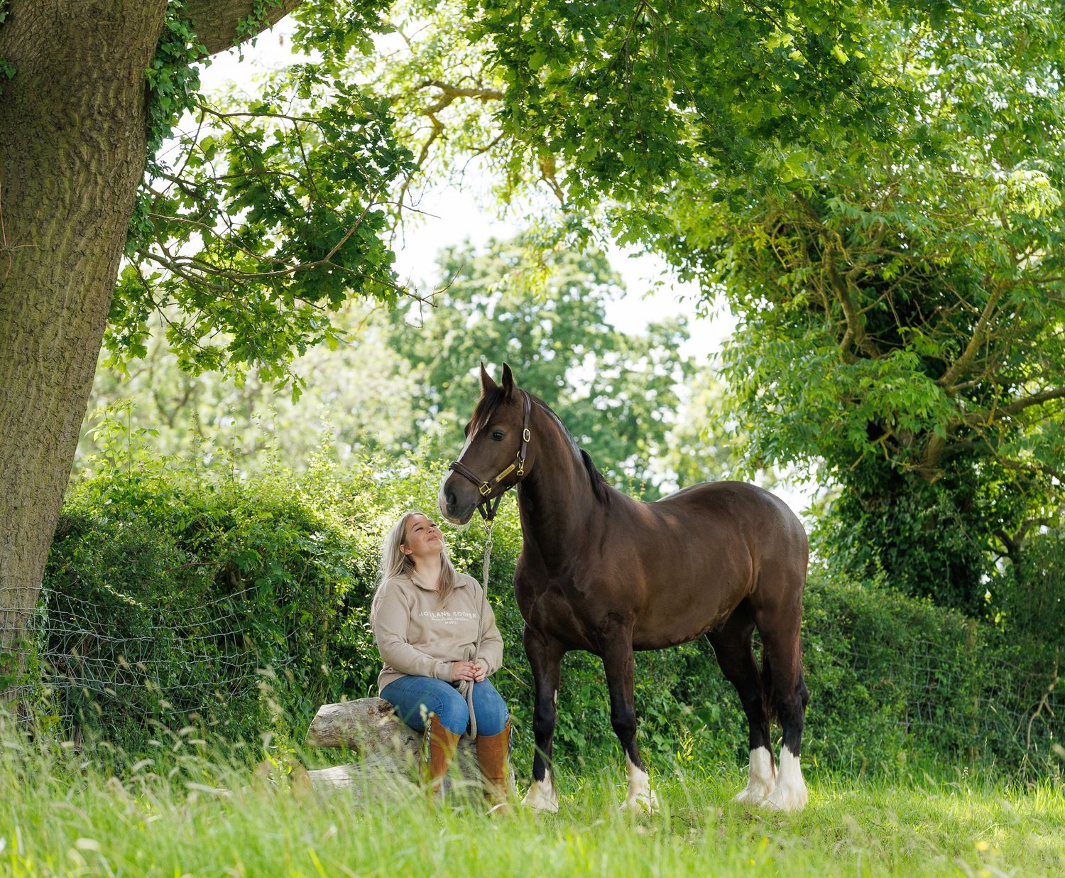 Two riders stand with their animals - a dog and a dark horse relaxing outdoors in a black and white photo.