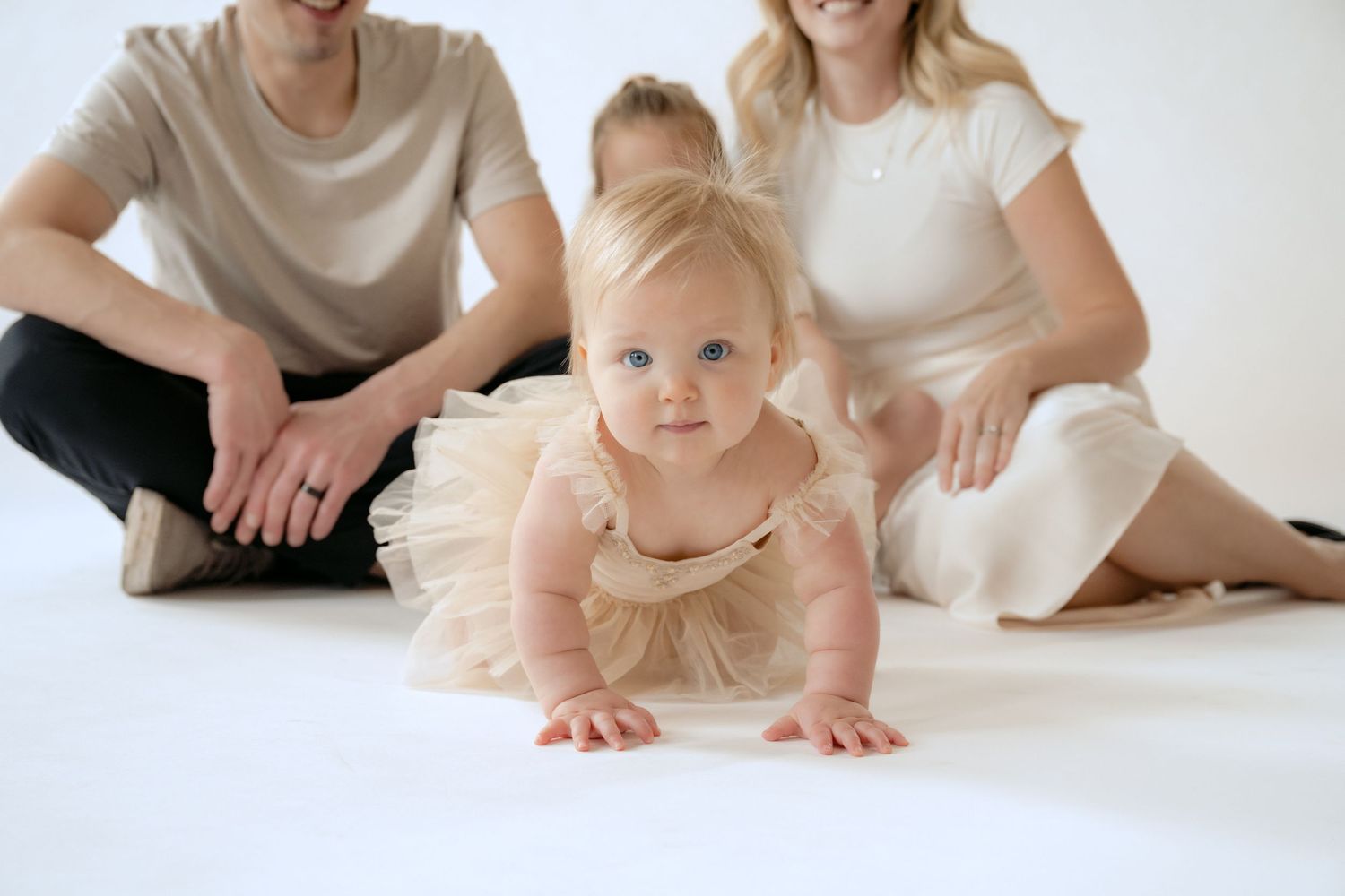 Close up of baby girl crawling towards the camera while her family sits in the background during in-studio family session in Stillwater MN.