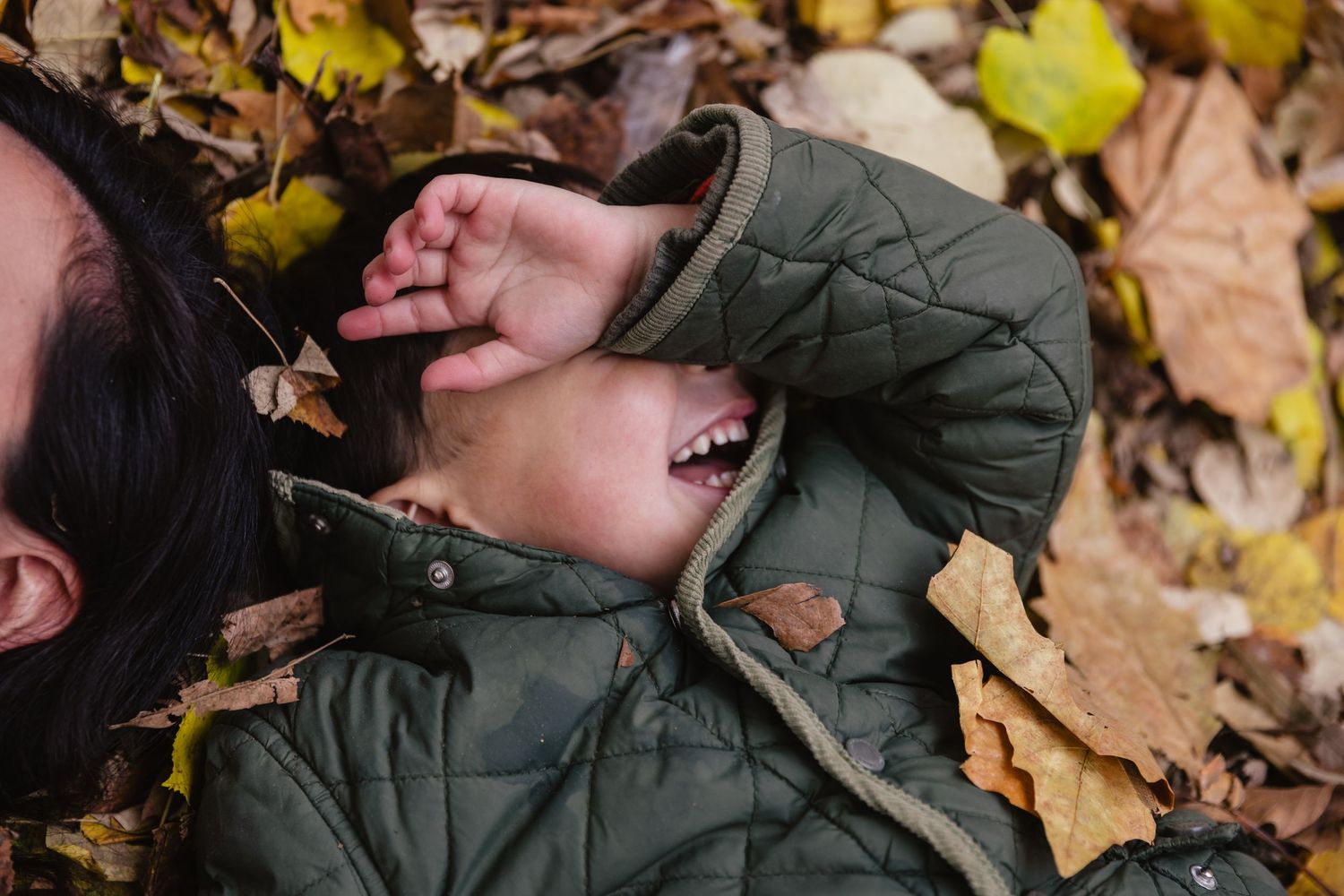 Un enfant rit aux éclats, couché dans un tas de feuilles mortes en automne