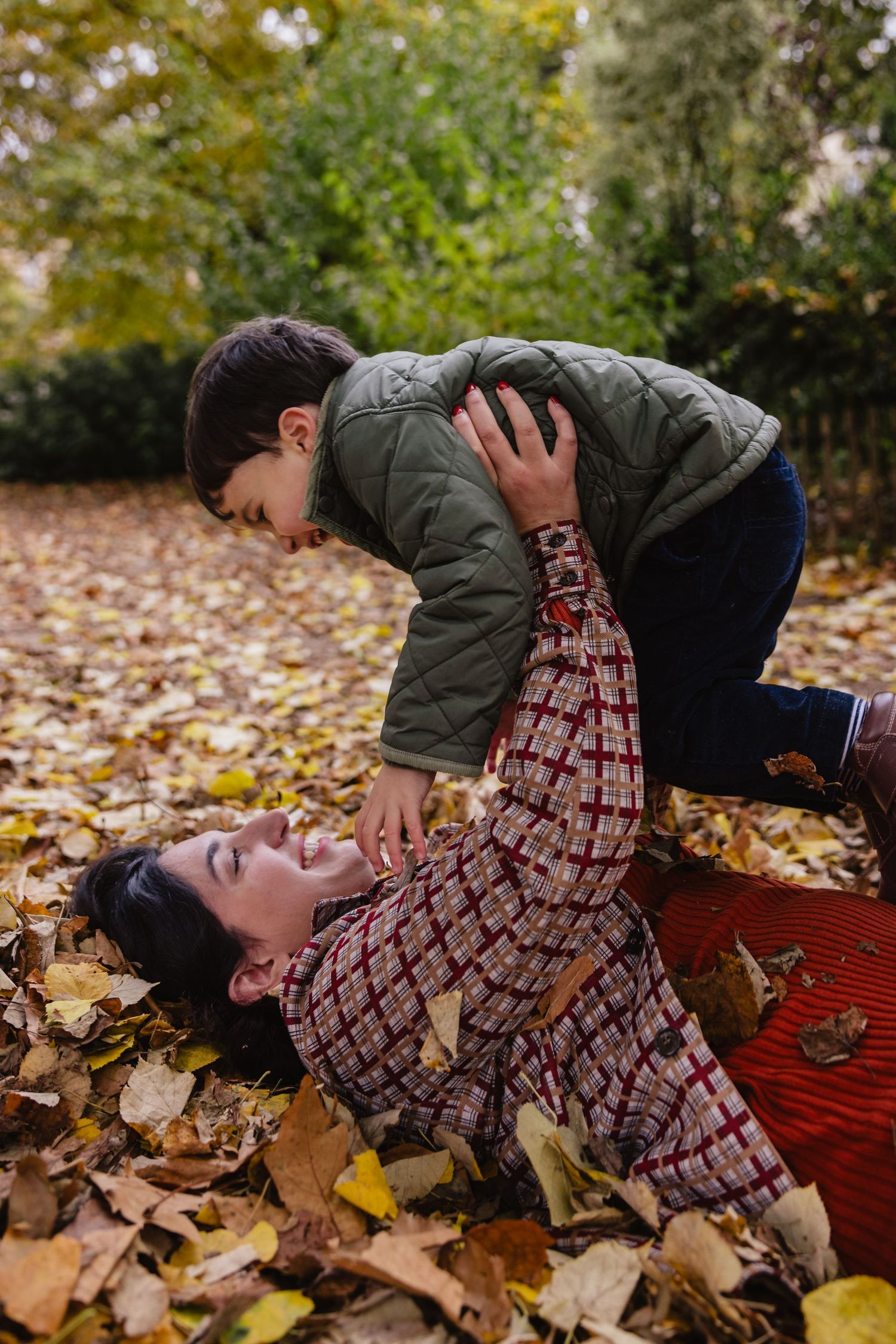 Une maman fait faire l'avion à son garçon dans un tas de feuilles d'automne.