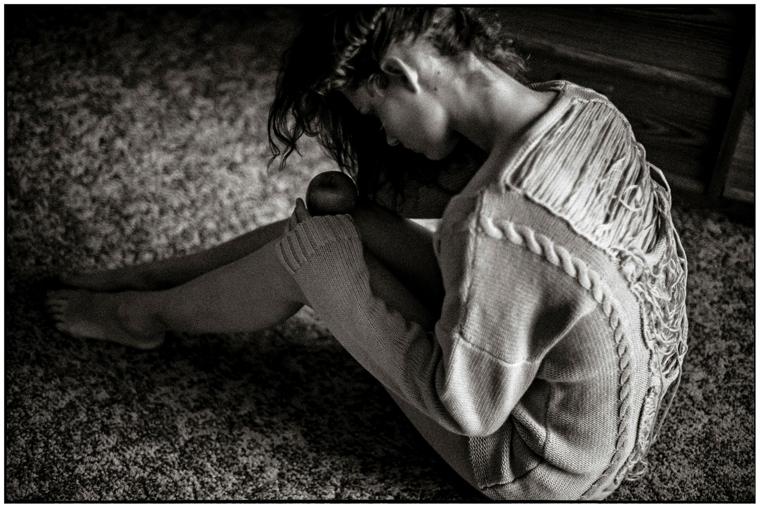 Black and white photo of a distressed young person sitting alone on floor, hugging knees in emotional pain.