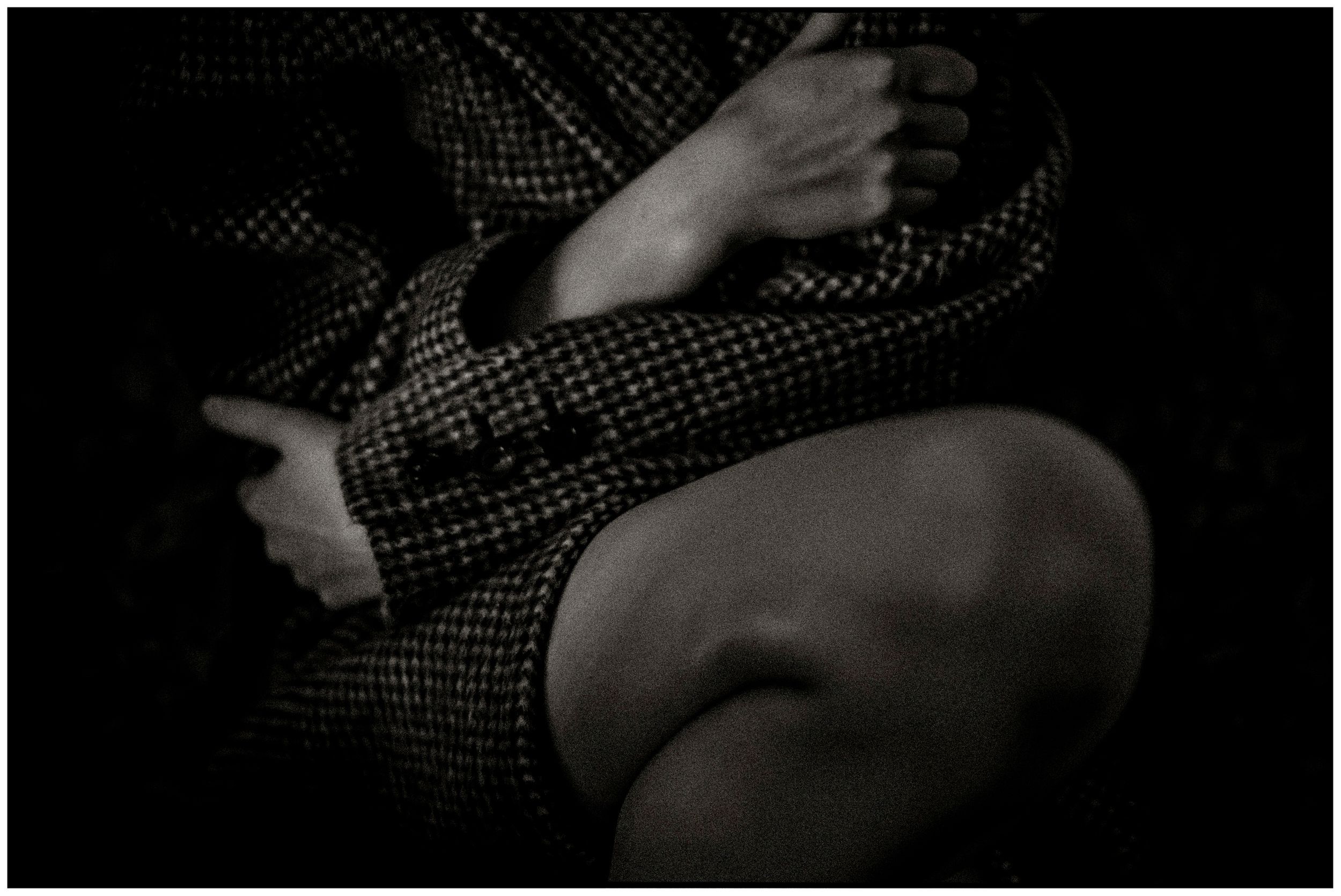 Black and white close-up of a person in a houndstooth jacket with crossed arms and bare knee.