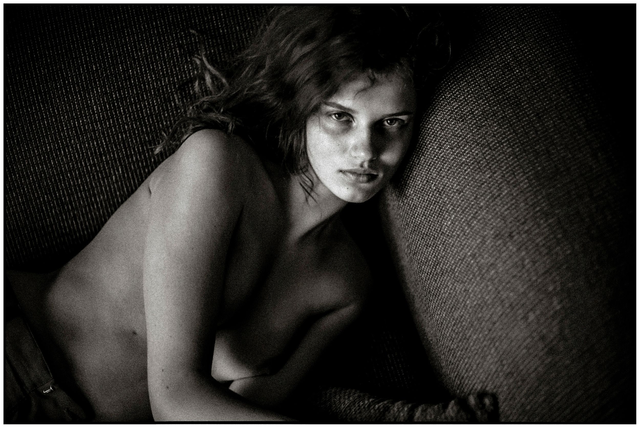 Black and white artistic portrait of a young woman in dramatic chiaroscuro lighting against textured background.