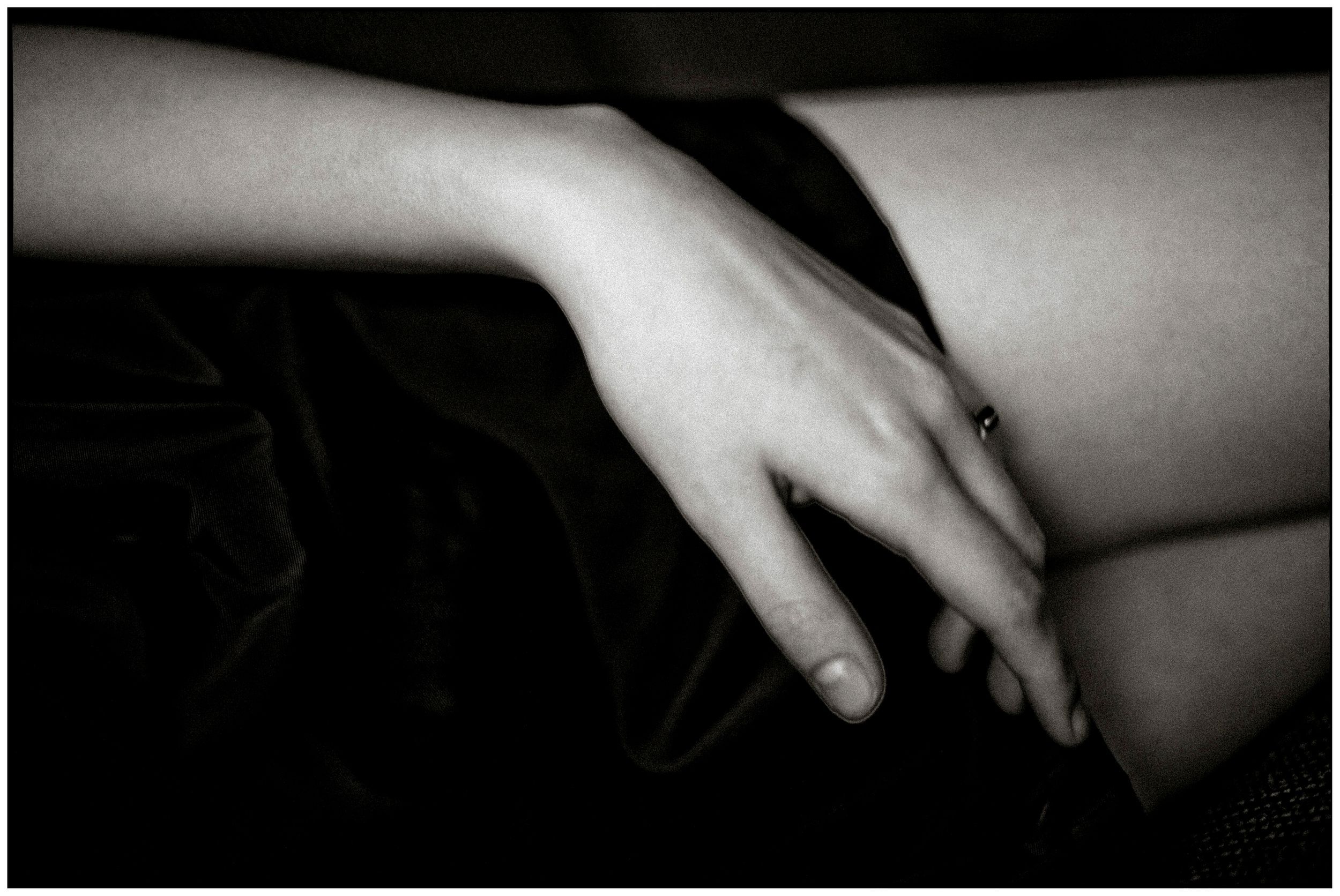 Close-up black and white photo of a womans hand resting gently on her leg in soft dramatic lighting.