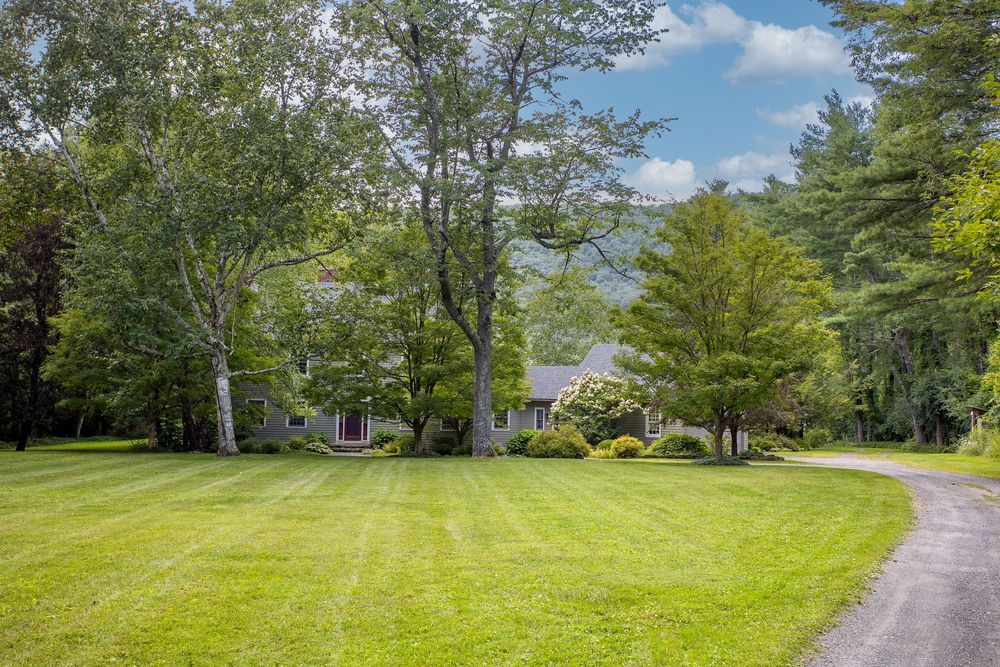 Charming country home with long driveway, manicured lawn, and mature trees in a serene setting.