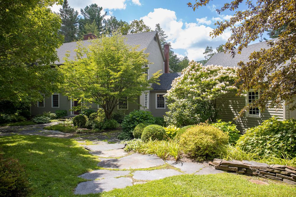 Stunning gray home with large arched window and balcony set among beautiful perennial garden landscaping.