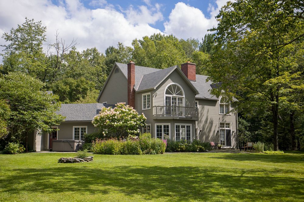 Sophisticated gray two-story home with balcony, arched window, and twin chimneys amid lush green lawn.