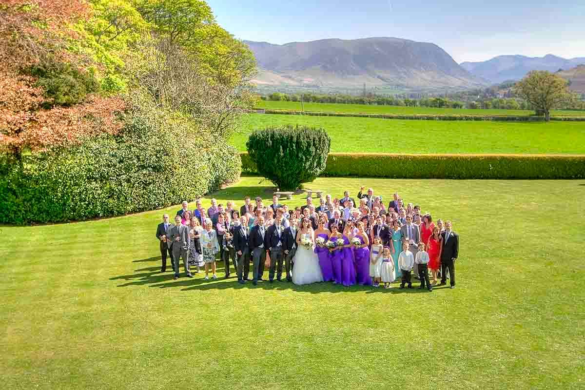 Aerial view of the wedding party posing on lawn at Hundith Hill Cockermouth with the Lake District in the background
